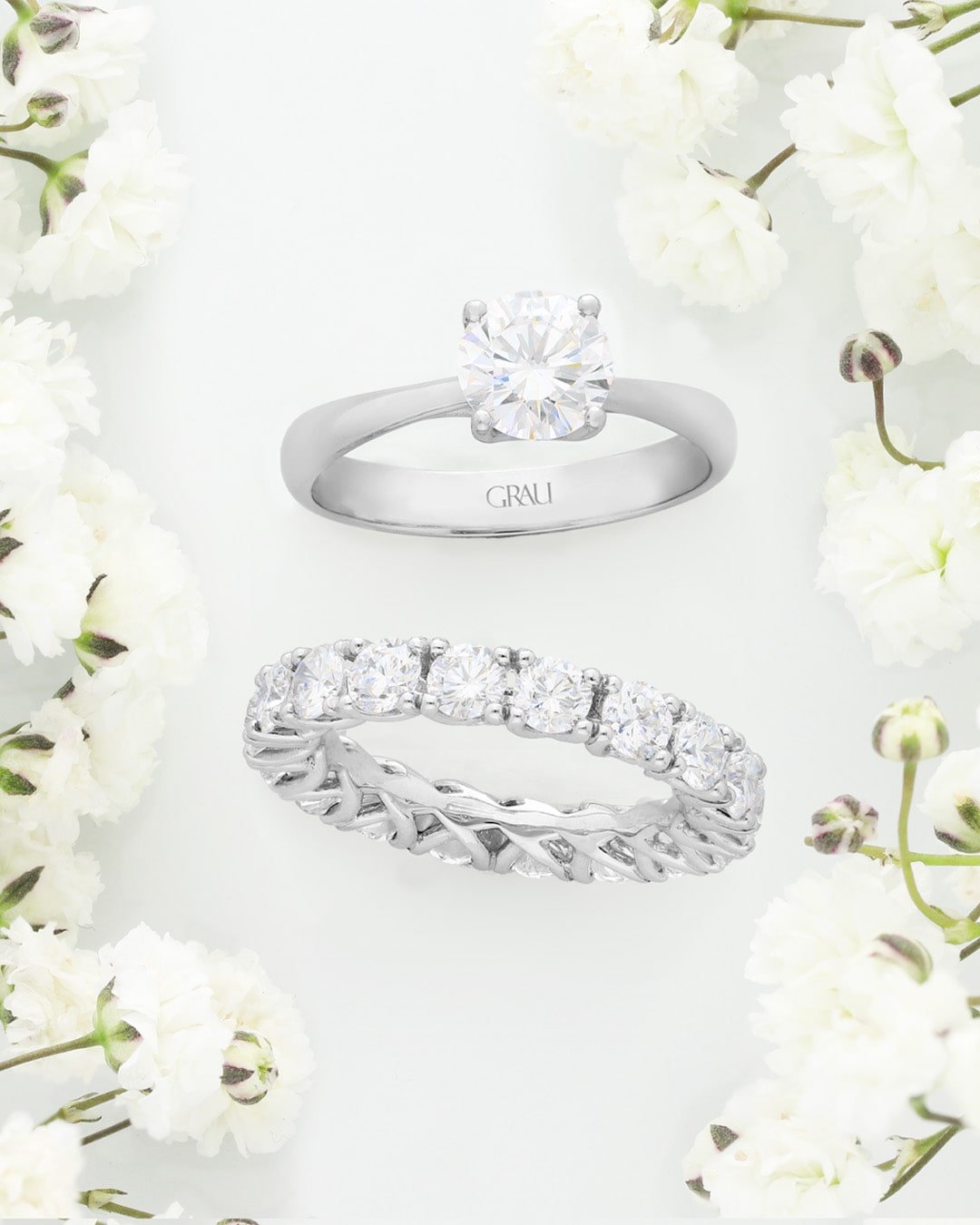 Anillo de compromiso y alianza de diamantes de Joyería Grau entre flores blancas