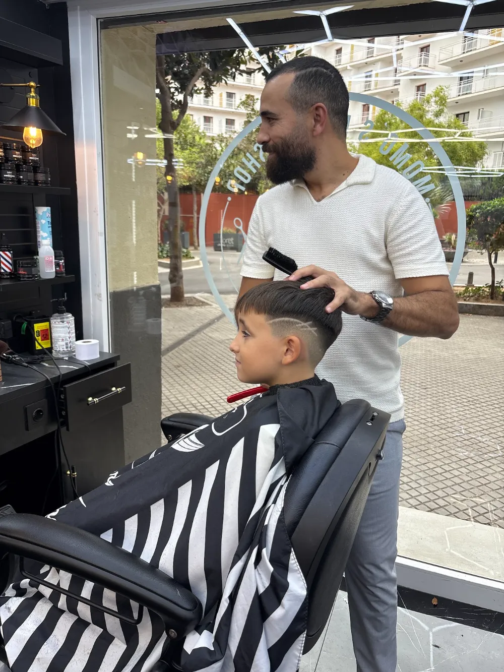 Barbero cortando el pelo a un niño con capa de rayas