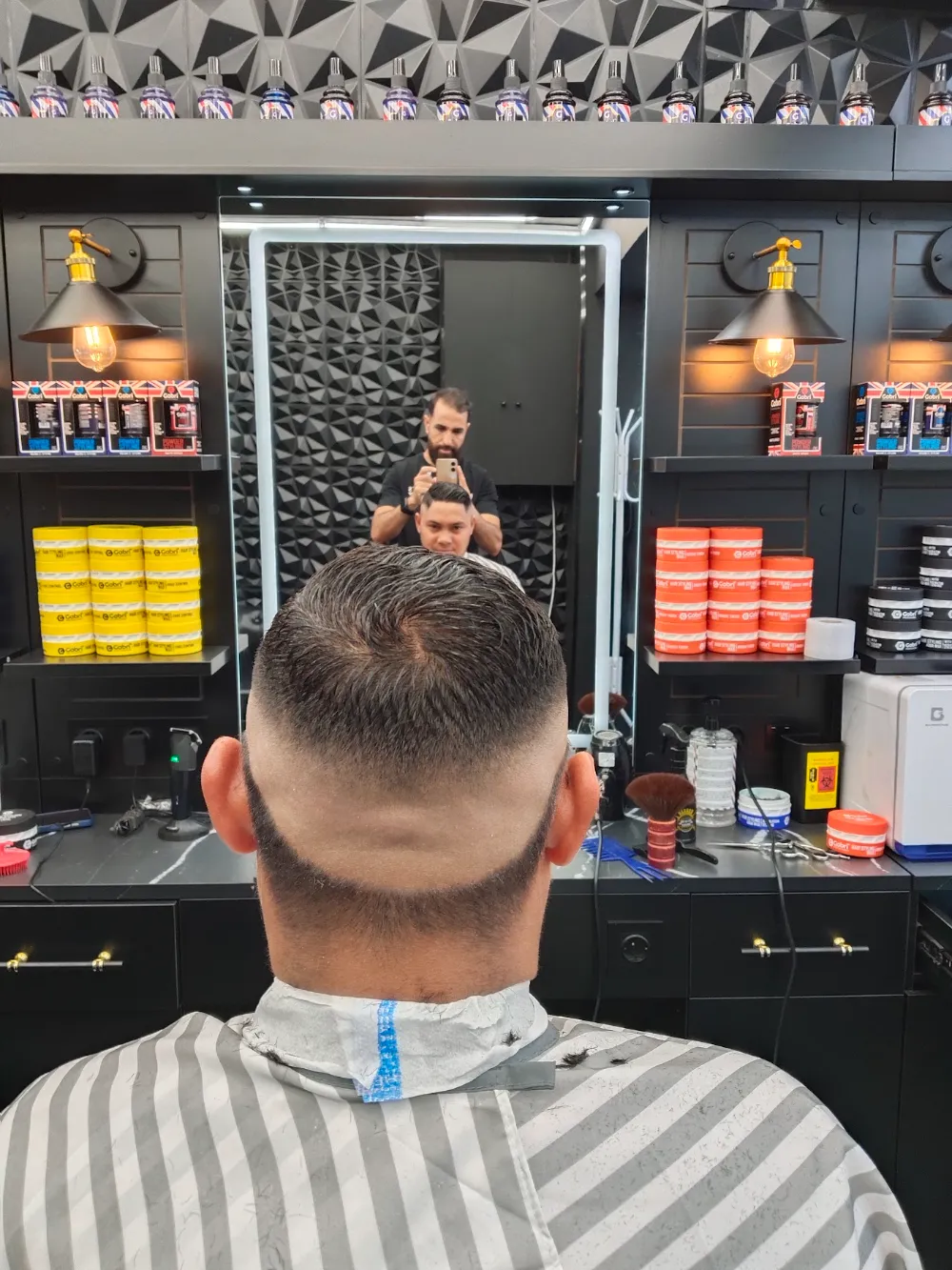 Cliente en el sillón visto de espaldas, reflejado en el espejo de la barbería