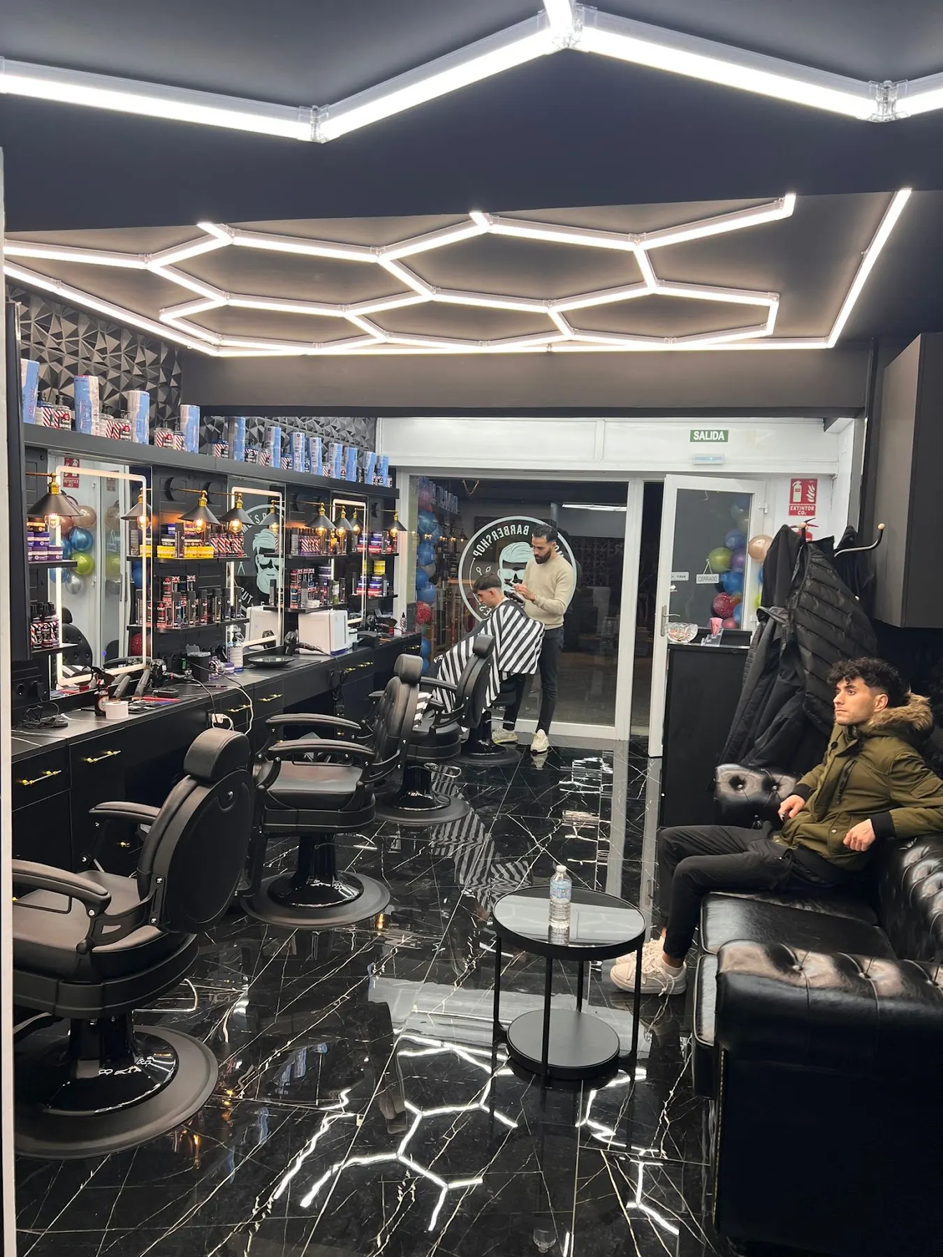 Interior de Momo's: techo con luces hexagonales, suelo de mármol negro y sillones de barbero