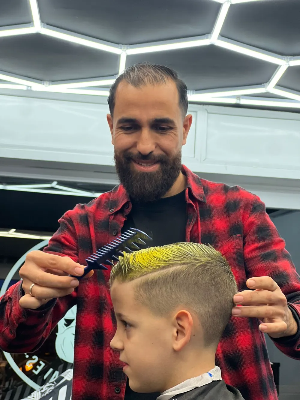 Barbero sonriendo mientras peina a un niño con el pelo pintado de amarillo con spray